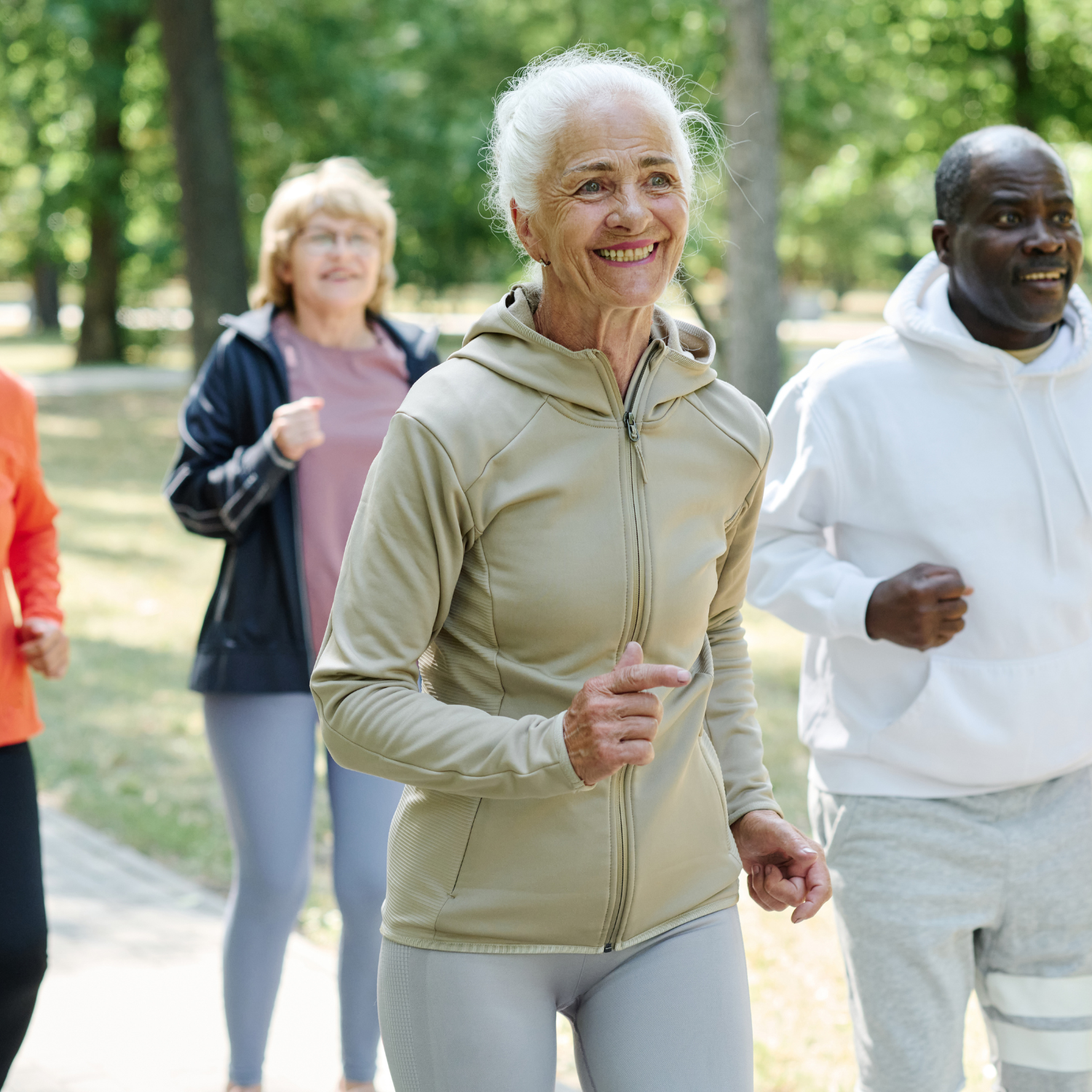 Four older adults walking together outdoors in a park, smiling and enjoying each other's company.